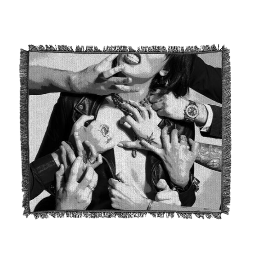 Black and white photograph of multiple hands reaching and grasping, printed on a fringed textile.